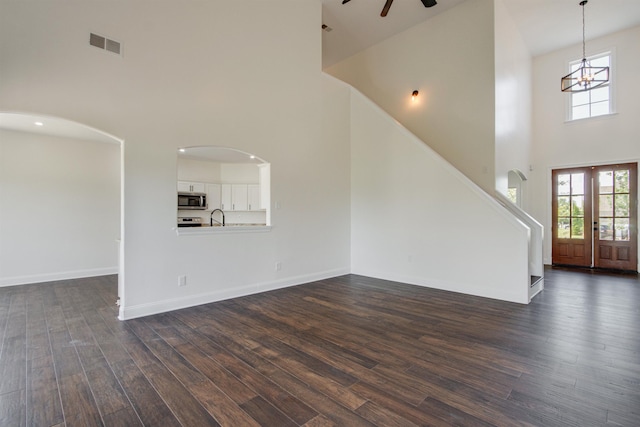 unfurnished living room featuring sink, dark wood-type flooring, a high ceiling, ceiling fan with notable chandelier, and french doors