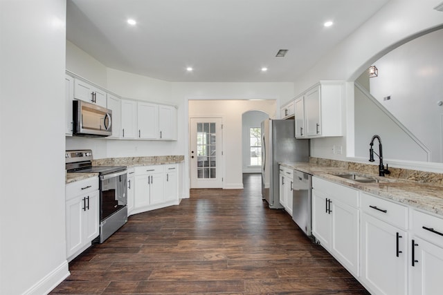 kitchen with sink, white cabinetry, stainless steel appliances, light stone countertops, and dark hardwood / wood-style flooring