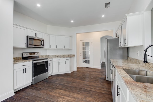 kitchen featuring appliances with stainless steel finishes, sink, white cabinets, dark hardwood / wood-style flooring, and light stone countertops