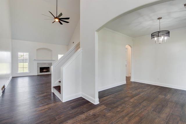 interior space with a towering ceiling, ceiling fan with notable chandelier, ornamental molding, a high end fireplace, and dark wood-type flooring