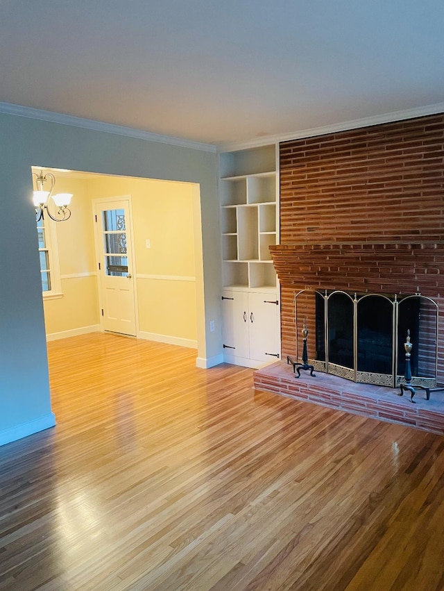 unfurnished living room featuring wood-type flooring, a brick fireplace, built in features, and crown molding