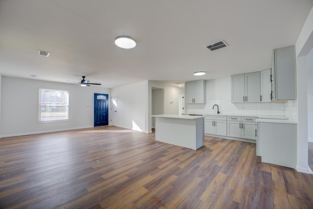 kitchen featuring dark wood-type flooring, sink, ceiling fan, a kitchen island with sink, and backsplash