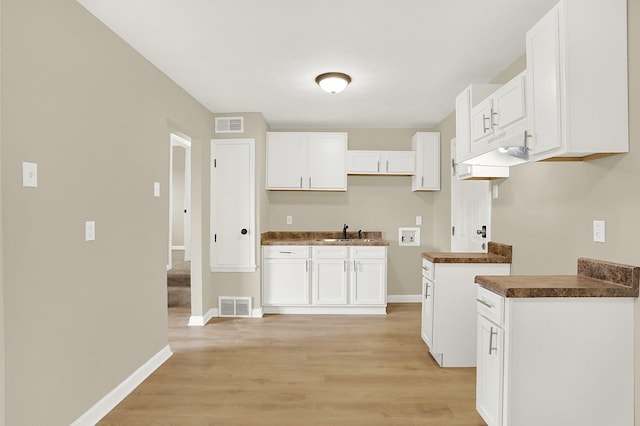 kitchen with white cabinetry, sink, and light hardwood / wood-style flooring