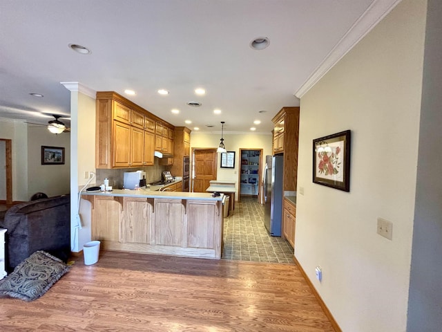 kitchen with stainless steel refrigerator, a breakfast bar, hanging light fixtures, light hardwood / wood-style floors, and kitchen peninsula