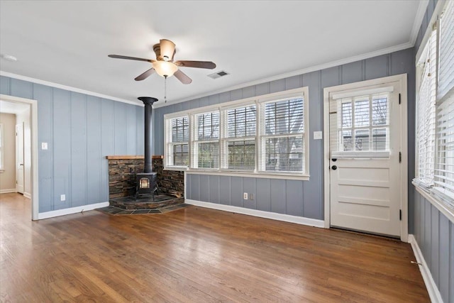 unfurnished living room featuring hardwood / wood-style flooring, ornamental molding, a healthy amount of sunlight, and a wood stove