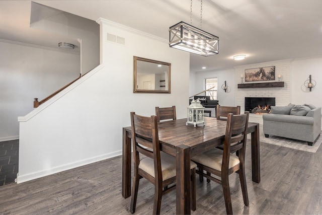 dining room with a brick fireplace, crown molding, and dark hardwood / wood-style floors