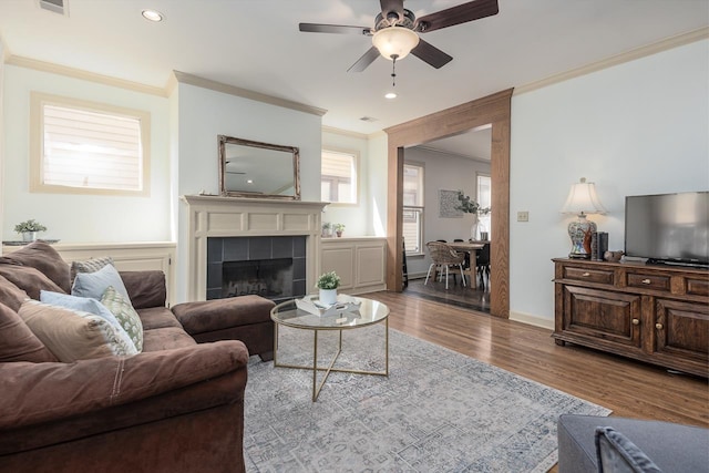 living room featuring hardwood / wood-style flooring, ornamental molding, a tiled fireplace, and ceiling fan