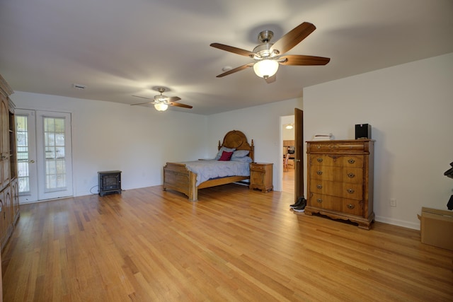 bedroom with french doors, light hardwood / wood-style flooring, access to outside, a wood stove, and ceiling fan