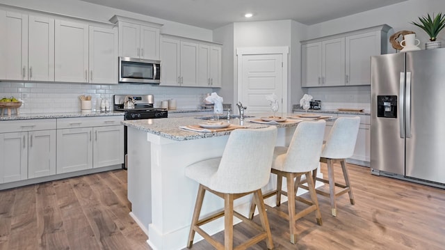 kitchen featuring appliances with stainless steel finishes, an island with sink, a breakfast bar area, light stone counters, and light wood-type flooring