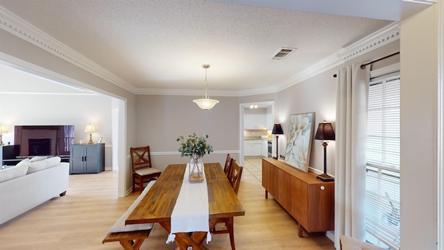 dining room with ornamental molding, a textured ceiling, and light hardwood / wood-style floors