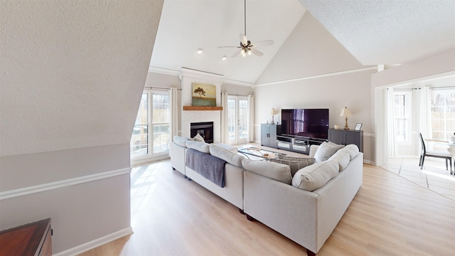 living room with light hardwood / wood-style flooring, ceiling fan, high vaulted ceiling, a fireplace, and a textured ceiling