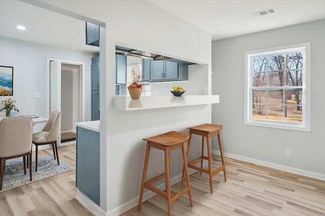 kitchen featuring blue cabinetry, kitchen peninsula, a kitchen breakfast bar, and light hardwood / wood-style floors