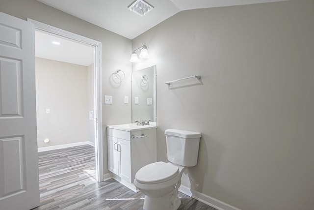 bathroom featuring vanity, wood-type flooring, lofted ceiling, and toilet