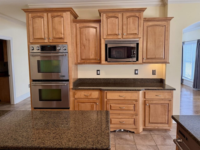 kitchen with stainless steel appliances, crown molding, and dark stone countertops