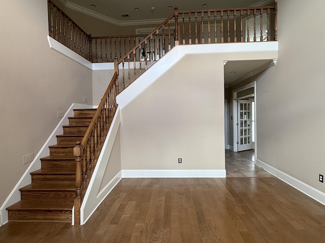 staircase featuring hardwood / wood-style floors, crown molding, and a towering ceiling