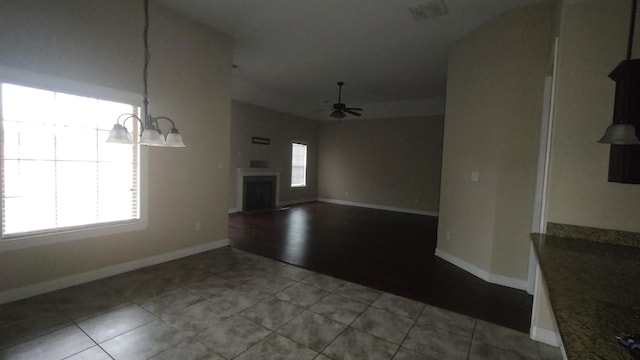 unfurnished living room with visible vents, ceiling fan with notable chandelier, a fireplace with raised hearth, and tile patterned floors