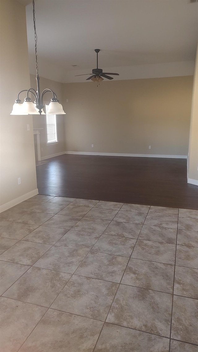 tiled empty room with ceiling fan with notable chandelier and baseboards