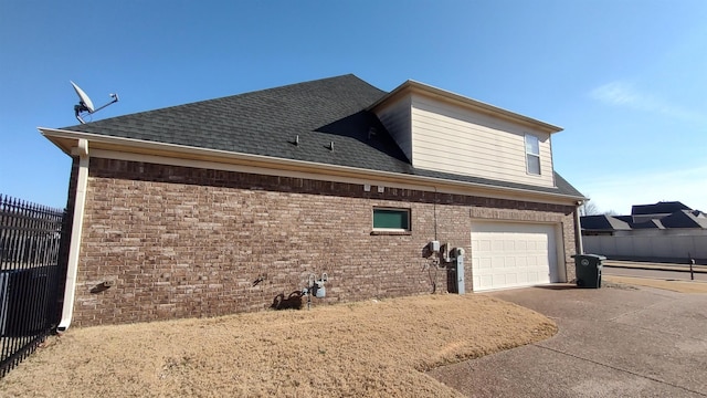 view of side of home featuring a shingled roof, fence, concrete driveway, and brick siding