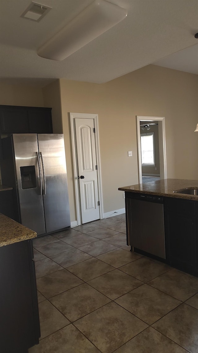 kitchen featuring stainless steel refrigerator with ice dispenser, lofted ceiling, visible vents, stone countertops, and dark tile patterned flooring