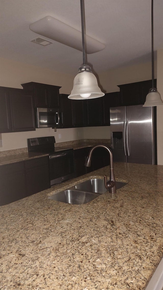 kitchen with stainless steel appliances, light stone countertops, sink, and decorative light fixtures