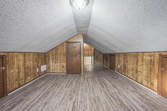 bonus room featuring wooden walls, dark hardwood / wood-style floors, vaulted ceiling, and a textured ceiling