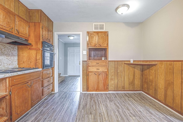 kitchen featuring stainless steel gas stovetop, oven, light hardwood / wood-style floors, and wood walls