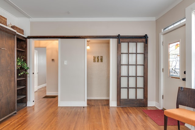 foyer entrance featuring crown molding, a barn door, and light hardwood / wood-style flooring