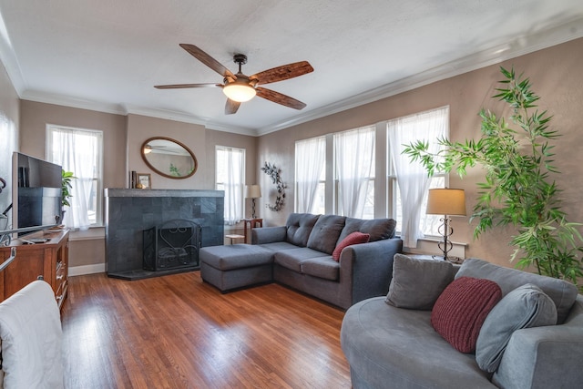 living room featuring a tiled fireplace, ornamental molding, ceiling fan, and dark hardwood / wood-style flooring