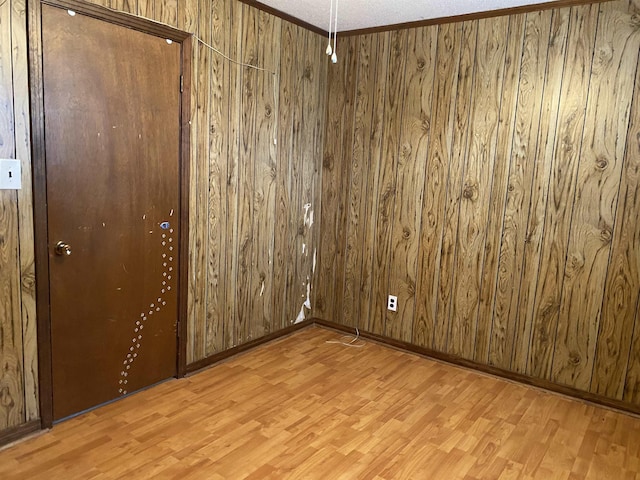 empty room with crown molding, wood walls, and light wood-type flooring