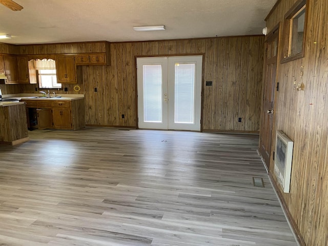 unfurnished living room featuring sink, light hardwood / wood-style flooring, wooden walls, heating unit, and french doors