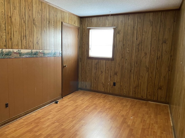 spare room featuring wood walls, light hardwood / wood-style flooring, and a textured ceiling