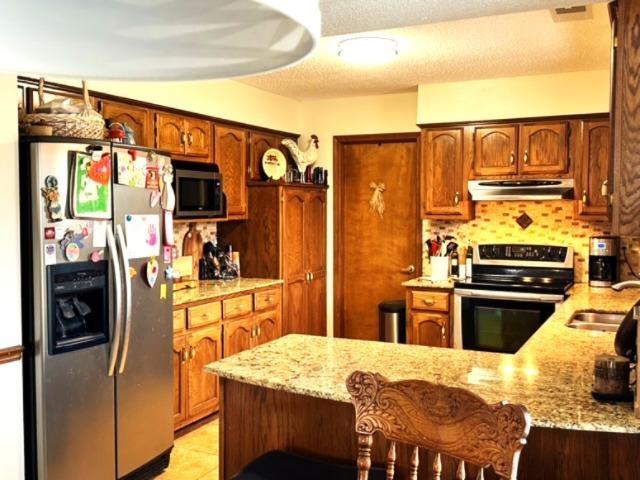 kitchen featuring tasteful backsplash, light stone countertops, kitchen peninsula, and appliances with stainless steel finishes