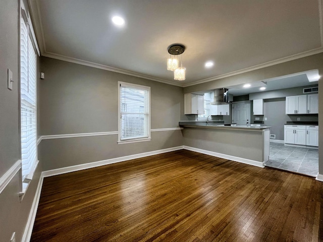 kitchen with decorative light fixtures, white cabinets, kitchen peninsula, dark wood-type flooring, and wall chimney range hood