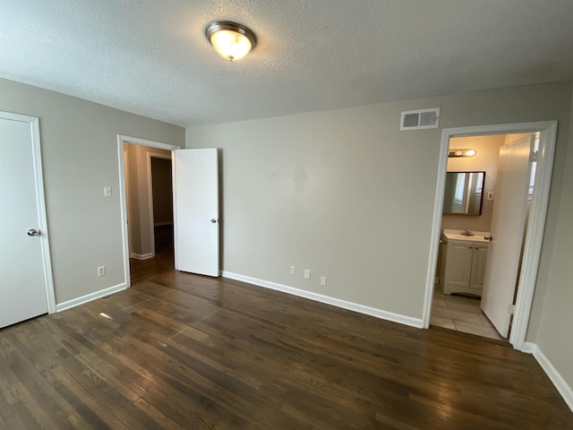 unfurnished bedroom featuring dark wood-type flooring, ensuite bath, and a textured ceiling