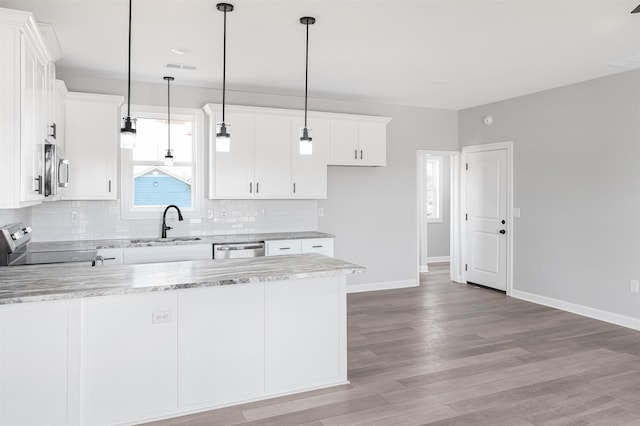 kitchen featuring appliances with stainless steel finishes, pendant lighting, white cabinetry, backsplash, and light stone countertops