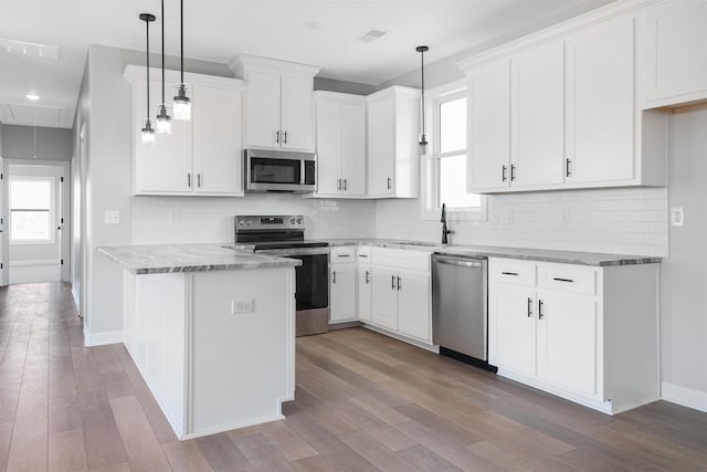 kitchen with stainless steel appliances, white cabinetry, light stone countertops, and decorative light fixtures