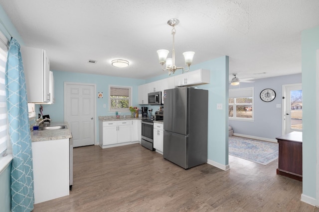 kitchen with appliances with stainless steel finishes, hardwood / wood-style floors, a wealth of natural light, pendant lighting, and white cabinetry