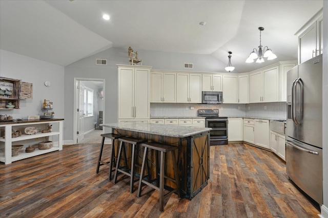 kitchen with a kitchen island, appliances with stainless steel finishes, lofted ceiling, hanging light fixtures, and light stone counters