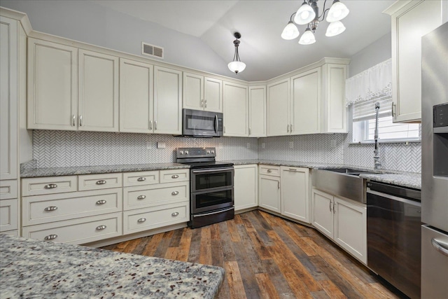 kitchen with pendant lighting, lofted ceiling, stainless steel appliances, tasteful backsplash, and light stone countertops