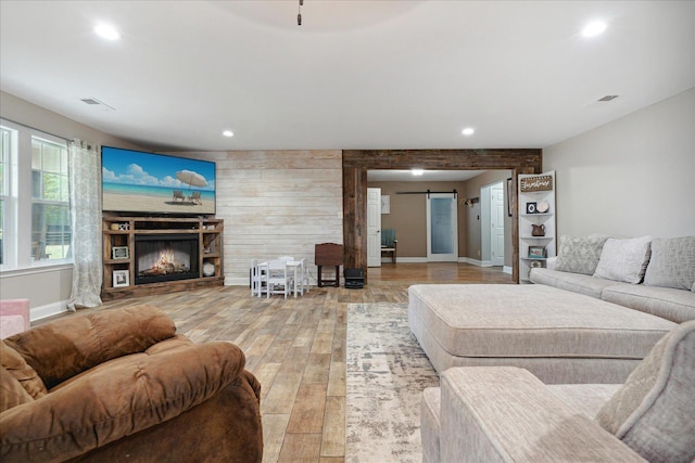 living room with a barn door, light hardwood / wood-style flooring, and wood walls