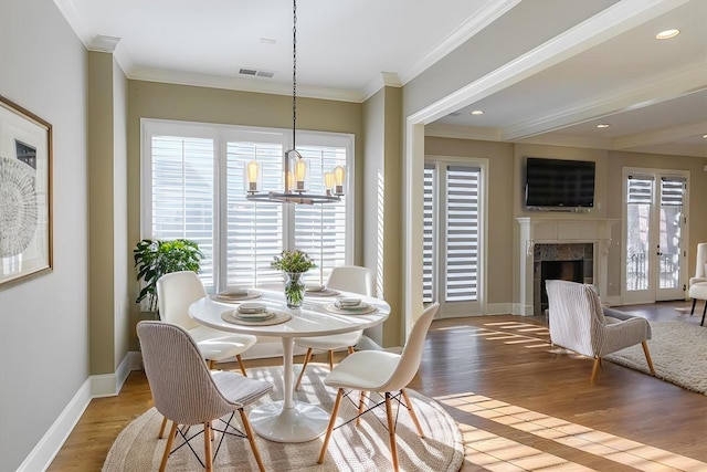 dining room with an inviting chandelier, a high end fireplace, wood-type flooring, and ornamental molding