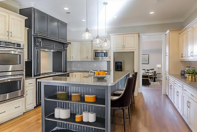 kitchen featuring an island with sink, appliances with stainless steel finishes, pendant lighting, and light stone counters