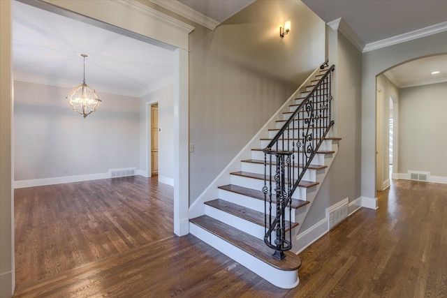 stairs featuring hardwood / wood-style flooring, ornamental molding, and an inviting chandelier