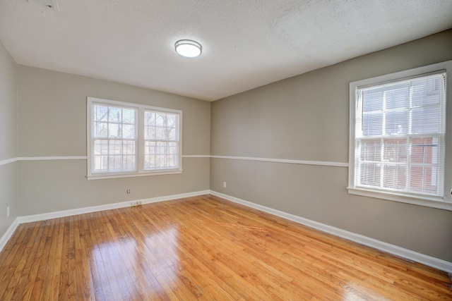 empty room with a healthy amount of sunlight, a textured ceiling, and light hardwood / wood-style flooring