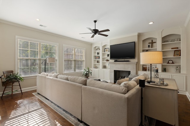 living room featuring ceiling fan, dark hardwood / wood-style floors, a fireplace, ornamental molding, and built in shelves