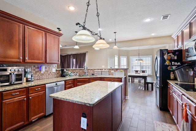 kitchen featuring appliances with stainless steel finishes, pendant lighting, sink, a center island, and kitchen peninsula