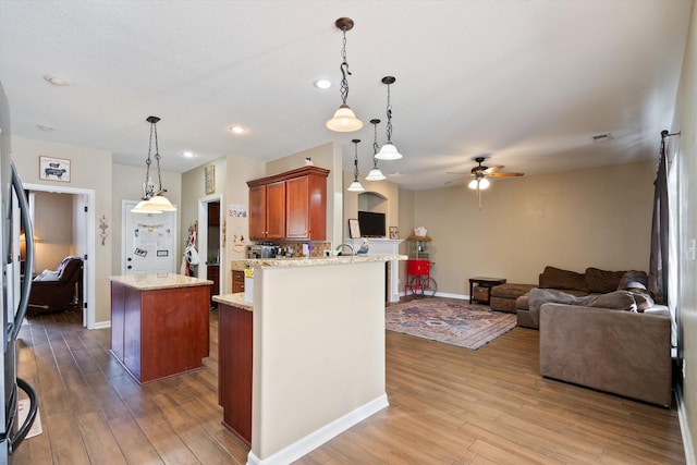 kitchen featuring decorative light fixtures, hardwood / wood-style flooring, light stone counters, kitchen peninsula, and ceiling fan