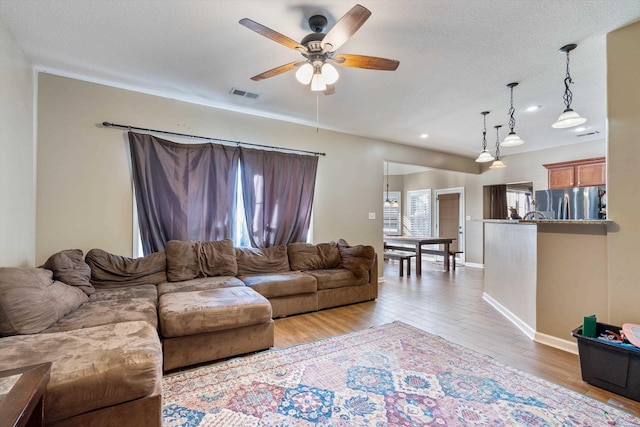 living room with a textured ceiling, ceiling fan, and light hardwood / wood-style flooring