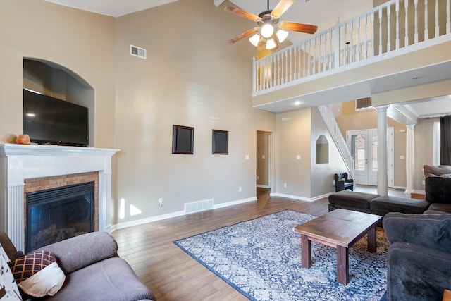 living room featuring french doors, ornate columns, a towering ceiling, hardwood / wood-style flooring, and ceiling fan