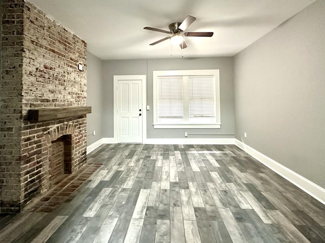 unfurnished living room with a brick fireplace, dark wood-type flooring, and ceiling fan